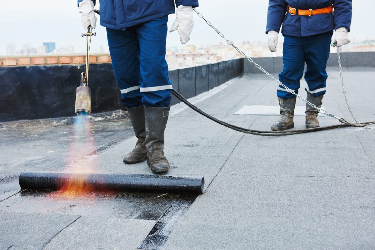 J5 roofers applying a flat roofing membrane during installation