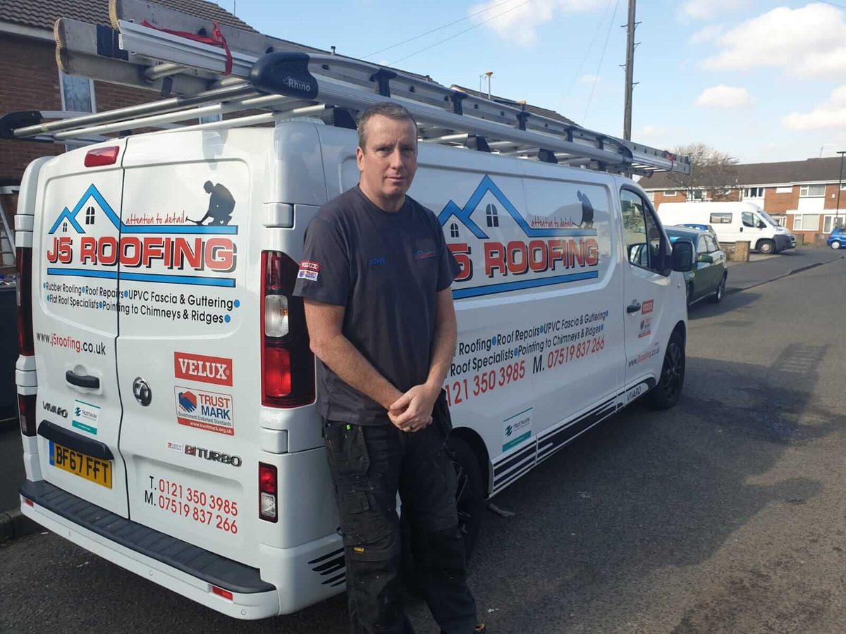 J5 Roofing team member standing beside branded company vans